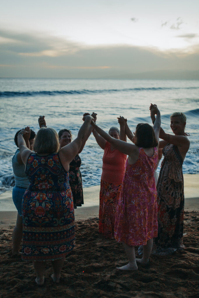 Women's circle on the beach in Maui, Hawaii with their arms up